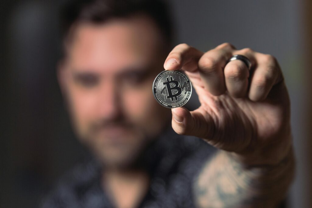 Persona che tiene una moneta Bitcoin in primo piano, con un focus sull'importanza e la popolarità delle criptovalute.