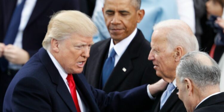 Donald Trump parla con Joe Biden, mentre Barack Obama osserva in secondo piano durante un evento ufficiale.