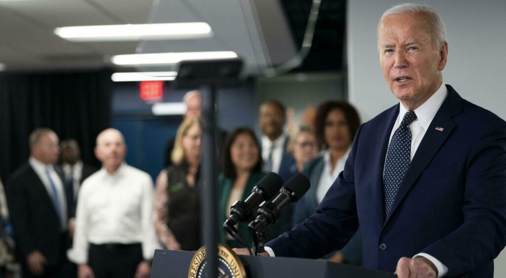 Joe Biden parla davanti ai microfoni durante un evento pubblico, con un gruppo di persone sullo sfondo